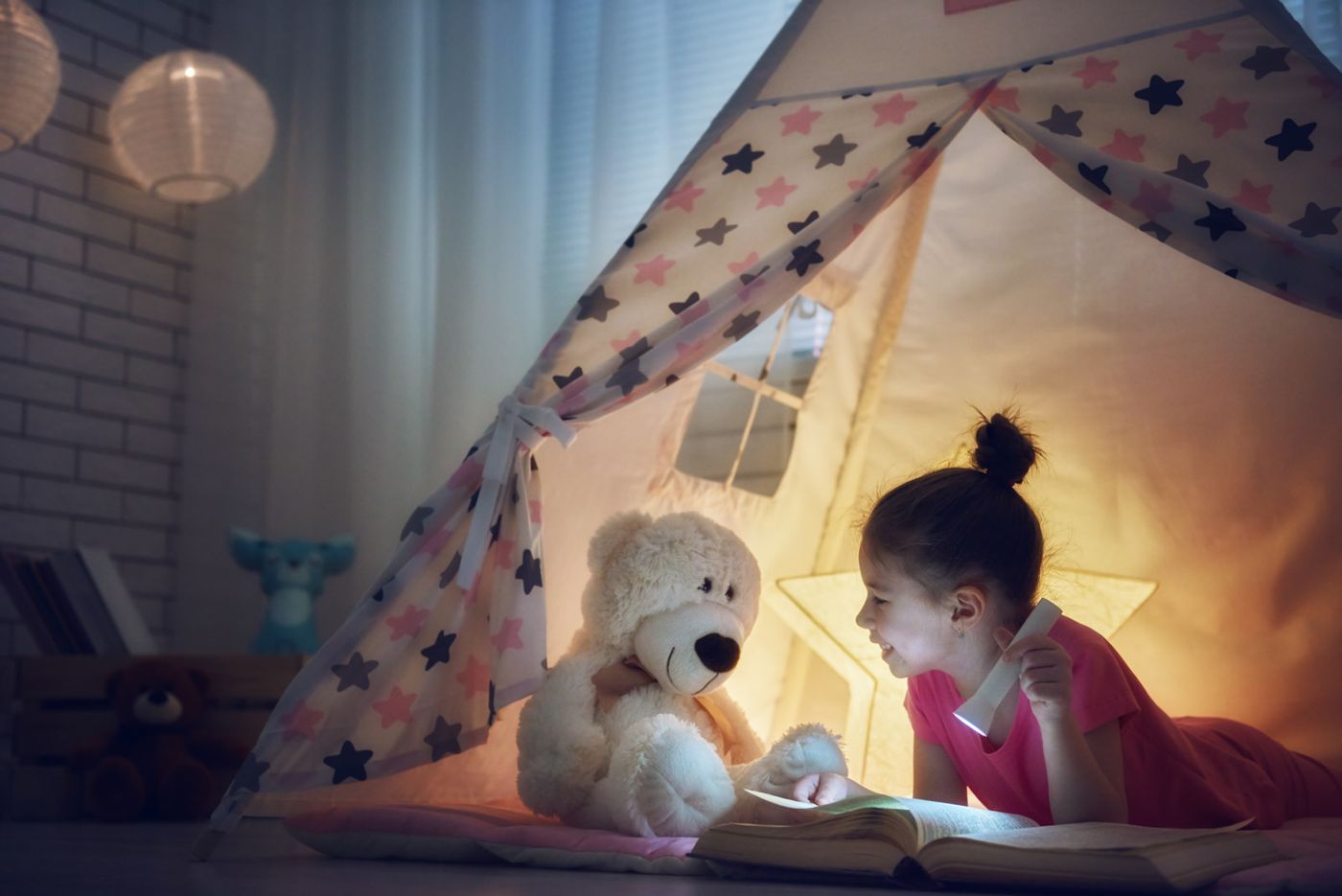 Meisje leest 's avonds met een zaklamp en haar knuffelbeer in een tentje in plaats van te slapen