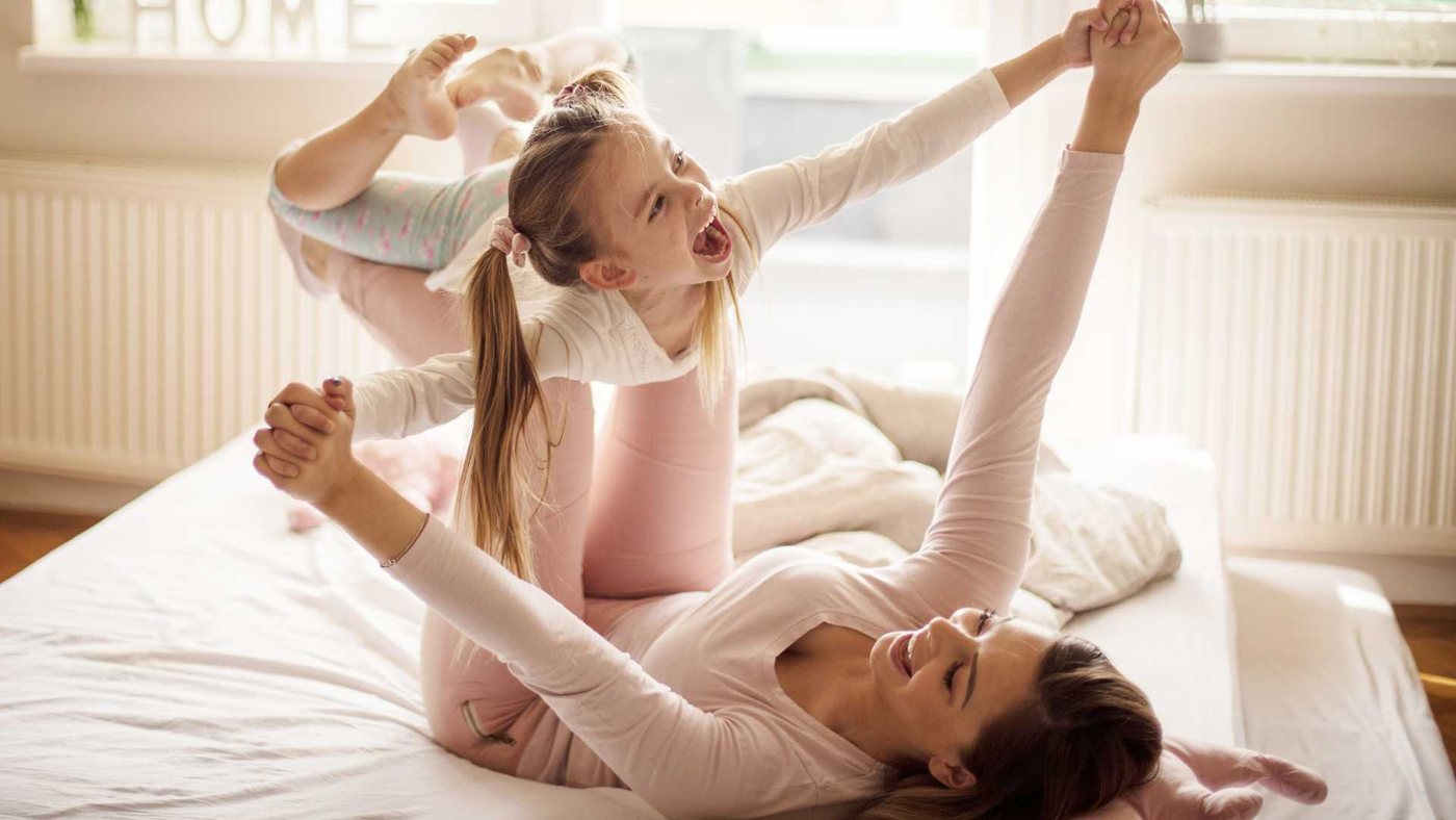 Moeder en dochter spelen lachend samen op bed: quality time met je strong-willed kind