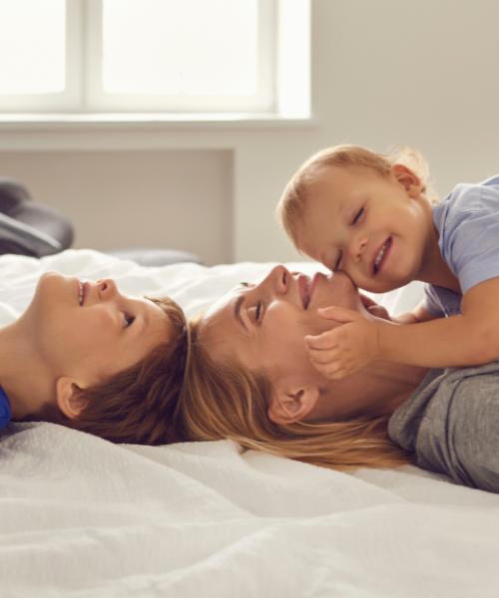 Moeder ligt lachend op bed met haar twee jonge kinderen dicht tegen zich aan