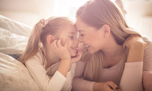 Moeder en dochter liggen lachend neus aan neus op bed