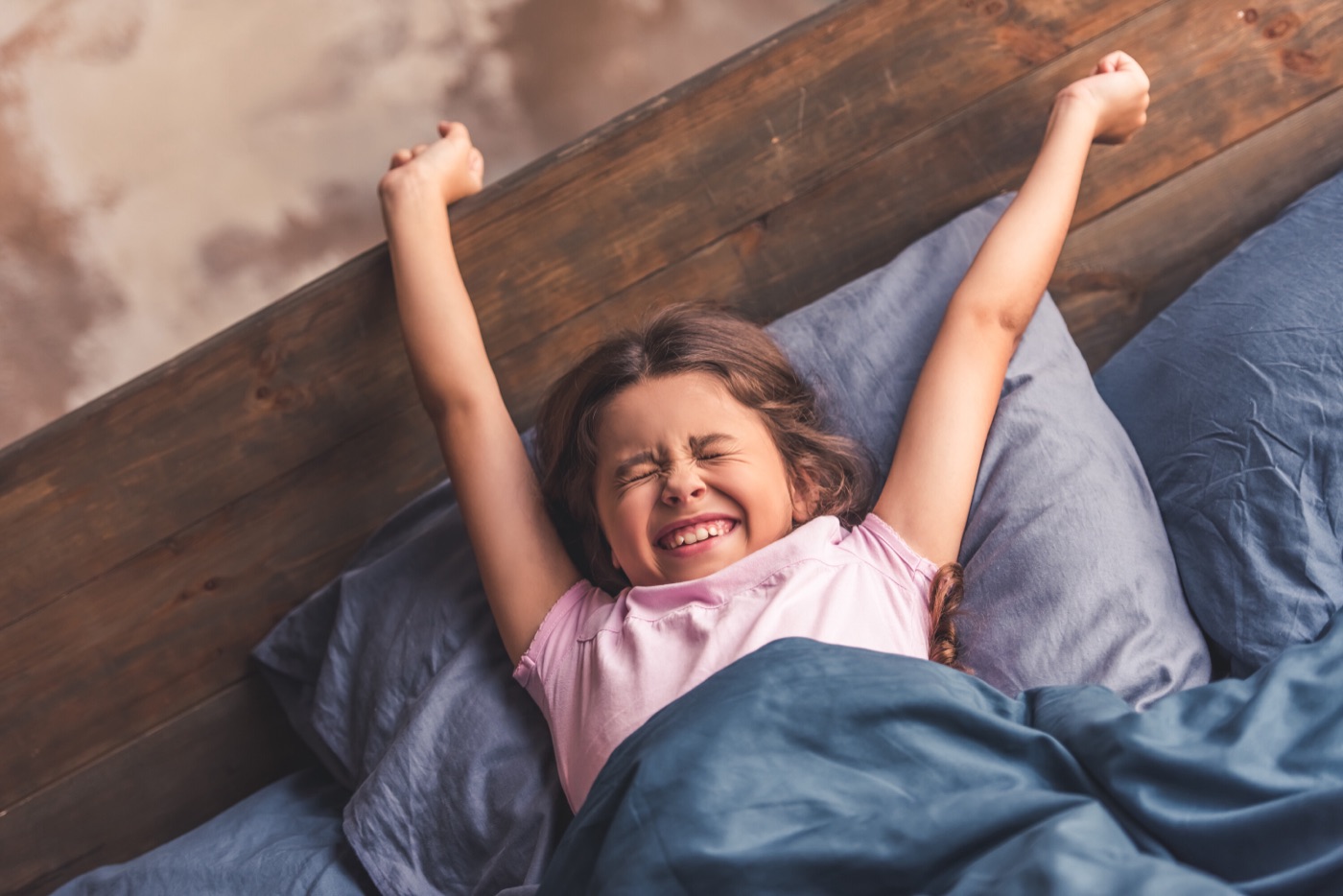 Meisje wordt uitgerust en blij wakker in haar eigen bed en rekt zich lachend uit