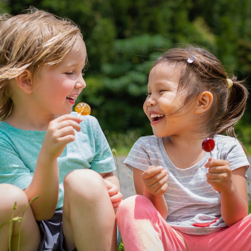 Twee kinderen zitten samen buiten te lachen met een lolly