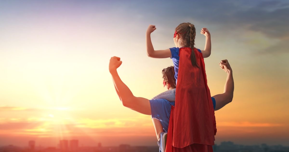 Ouder en kind in superheldencapes laten samen hun spierballen zien bij zonsondergang